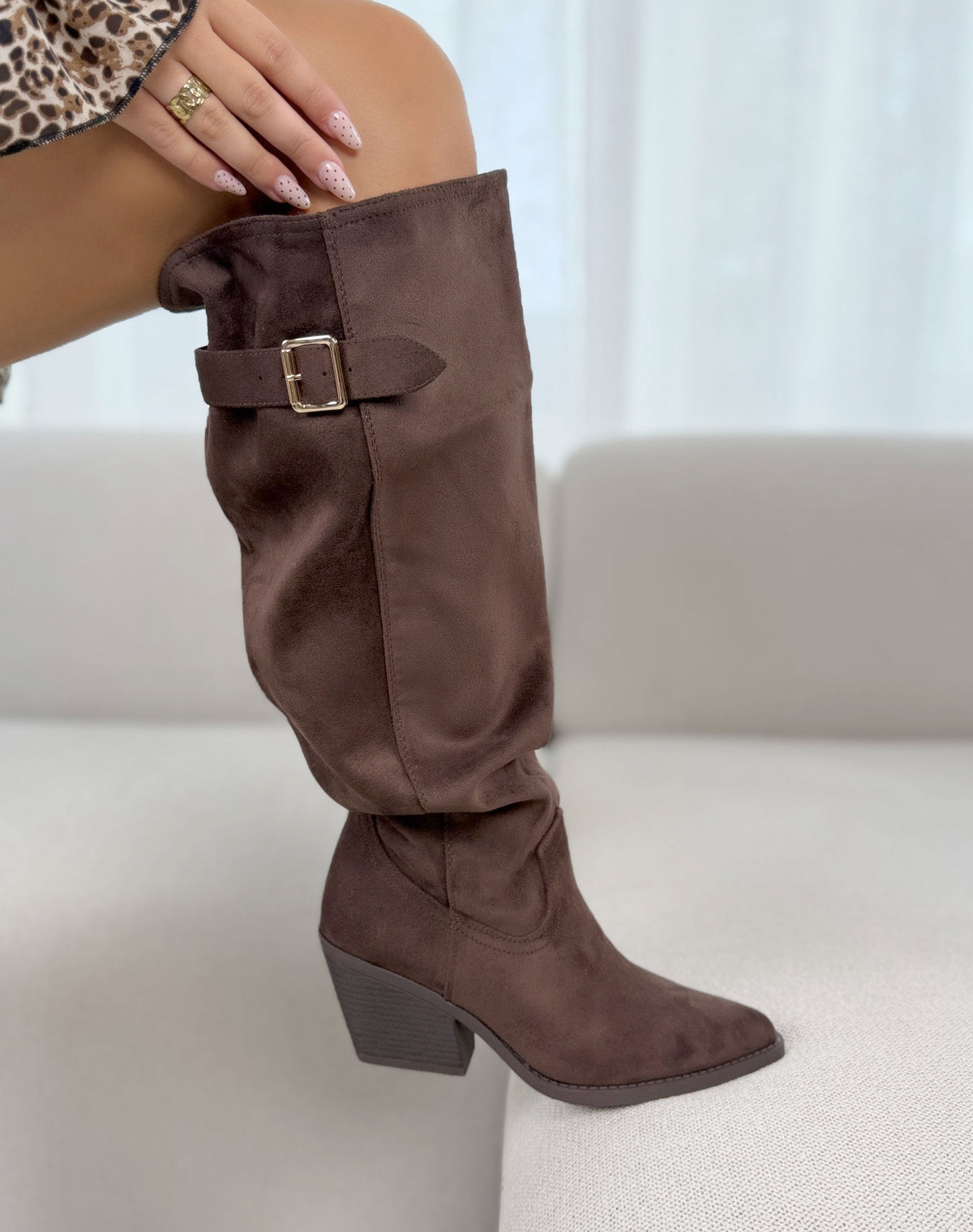 Bottes marron en suédine à tige large avec sangle ajustable à boucle dorée. Le modèle possède un bout pointu et un talon épais biseauté.